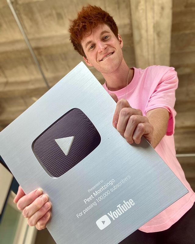 Peet Montzingo in a pink t-shirt holding a silver YouTube play button.